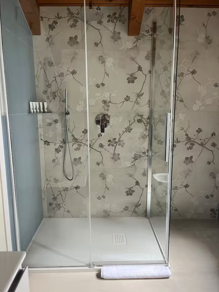 Glass-enclosed shower in the first bathroom with a delicate floral wall finish