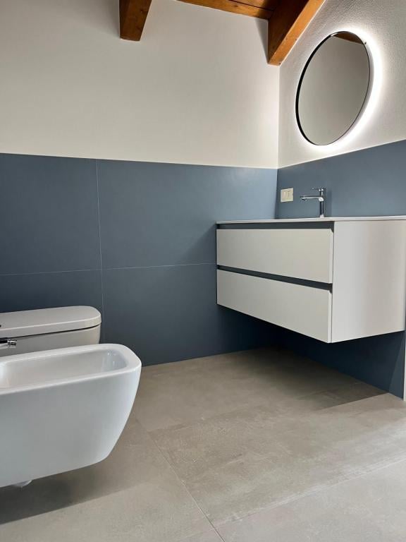First bathroom with a floating vanity, illuminated round mirror, wall-mounted toilet and bidet